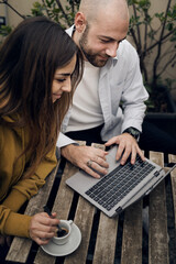 Couple of young people using laptop outdoors - best friends surfing the web sitting at outdoors...