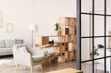 Interior of light living room with wooden bookcase and grey armchair