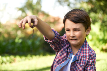 Eww. Shot of a cute little boy holding up an earthworm he found in the garden.