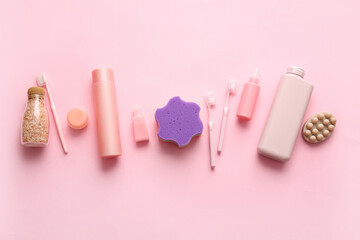 Bottles of cosmetic products and different bath supplies on pink background