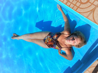 Caucasian mature woman wearing a bathing suit indoors lying on the ladder of a swimming pool