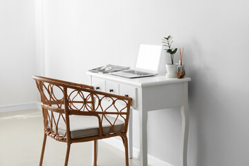 Modern workplace with laptop and wicker chair near light wall