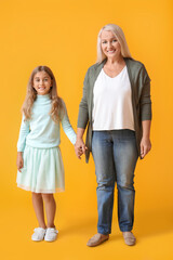 Mature woman with her little granddaughter holding hands on yellow background