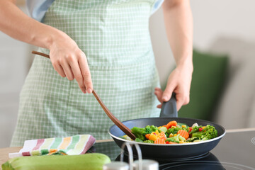 Housewife with spatula frying vegetables in kitchen, closeup