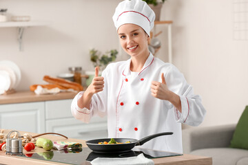 Female chef showing thumbs-up near frying pan with vegetables in kitchen - Powered by Adobe