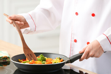 Female chef with spatula frying vegetables in kitchen, closeup