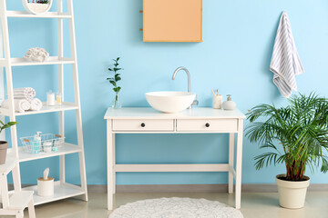 Interior of stylish bathroom with sink, shelving unit and blue wall