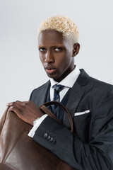 blonde african american man with blue eyes holding leather bag isolated on grey