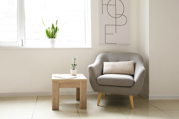 Grey armchair with table and houseplants near light wall