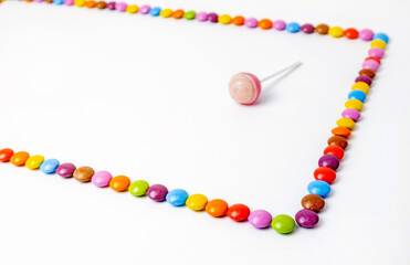 Chocolate dragees lined with rectangle on white background. Frame of colorful candies with lollipop.