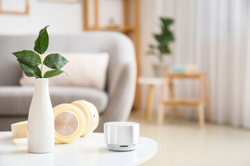 Fototapeta na wymiar Wireless portable speaker, headphones and vase with plant branch on table in room
