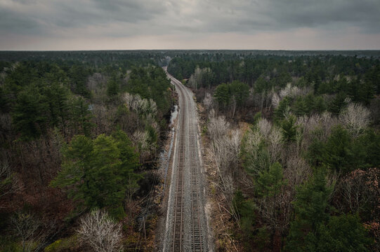 An aerial view of train tracks running through a dense green forest off into the horizon on a cloudy autumn day in Severn Falls, Ontario, Canada.