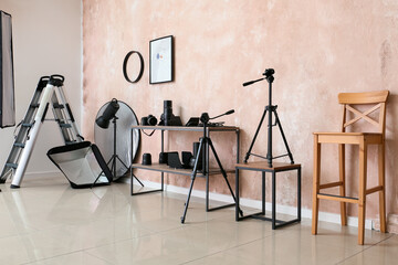 Shelving unit with lighting equipment and chair near pink wall in photo studio