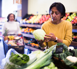 Latin american female shopper choosing fresh cabbage head in vegetable department of supermarket....