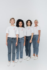 Obraz premium Interracial women with pink ribbons on t-shirts looking at camera on grey background.