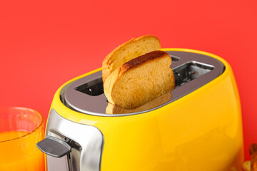Modern toaster with bread slices and glass of juice on red background, closeup