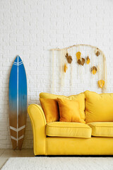 Comfortable sofa and surfboard near white brick wall
