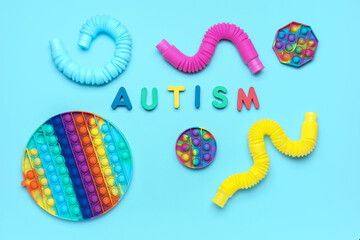 Word AUTISM with pop it fidget toys and tubes on blue background
