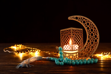 Arabic candle holder with glowing candle, garland and tasbih on table against dark background