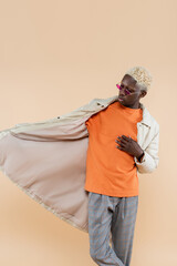 young african american man in stylish sunglasses and coat isolated on beige