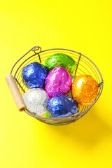 Basket with chocolate Easter eggs on yellow background