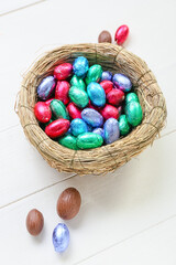 Nest with chocolate Easter eggs on light wooden background