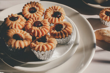 Tasty cookies with jam on top in white plates and hot coffee with window light. Breakfast. Close up. Vintage tone