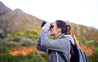 Getting a better view. Shot of an attractive young woman looking through binoculars while on a hike.