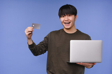 Smiling happy asian korean young boy man student holding credit card for online shopping,...