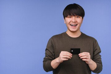 Closeup portrait of a smiling young asian man korean boy holding showing credit card for loan,...