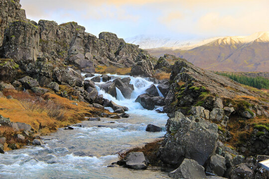 A beautiful mountain creek rushes with water in Iceland in a picturesque setting that is illuminated by beautiful colorful light with snow in the distance - Powered by Adobe