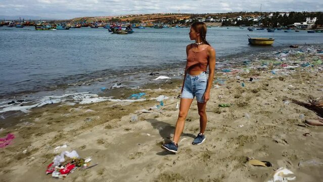 Slim Woman Looking In The Coast Of Mui Ne While Walking At Beach With Garbage In Vietnam. - aerial pullback
