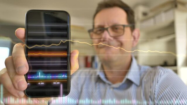 Happy Businessman with glasses holding smartphone with glowing candlesticks showing stock market trade