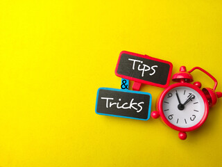 Top view wooden board and alarm clock with text Tips and Tricks on yellow background.