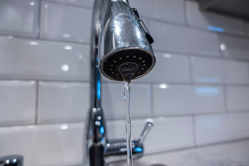 Low angle, selective macro focus on a stainless steel kitchen sink faucet, with water pouring in a thin steady stream