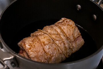 Close up, selective focus on a juicy, pork chashu roast cooking in a large pot filled with soy sauce and green onions