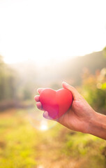 Hand holding heart against a golden sunset.