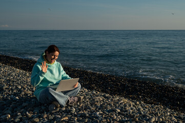 Caucasian woman communicating by video call on laptop on pebble beach. 