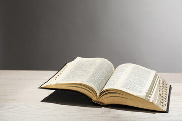 Open Bible on white wooden table against light grey background. Christian religious book