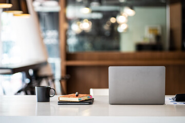 Simple workspace laptop and notebook on white table with blurred office room background.
