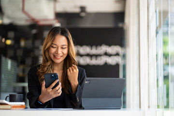 Smiling Asian businesswoman using phone in office. Small business entrepreneur looking at her...