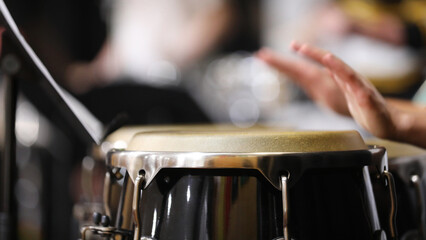 A close up of hands moving or in motion playing the congas or bongo style drums in a percussion section of a band or orchestra. Drum skin in focus.