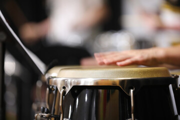 A close up of hands moving or in motion playing the congas or bongo style drums in a percussion section of a band or orchestra. Drum skin in focus.