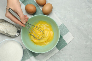 Woman whisking eggs in bowl at grey table, top view. Space for text