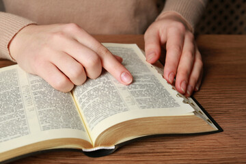 Fototapeta premium Woman reading Bible at wooden table, closeup