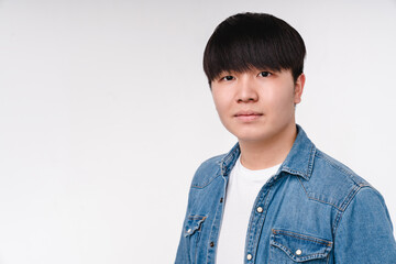 Serious young asian korean boy man student in denim shirt looking at the camera isolated on white. Closeup cropped portrait