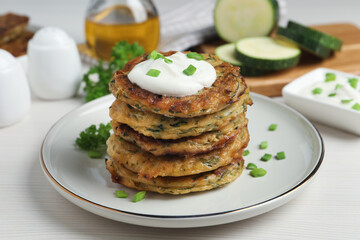 Delicious zucchini pancakes with sour cream served on white wooden table
