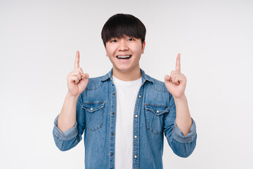Smiling young korean asian man boy with teeth braces showing pointing at copyspace free space for advertise upwards isolated on white background