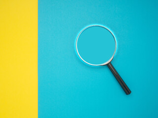 Top view of a magnifying glass on a yellow and blue background