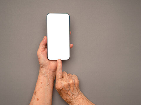 Top View Of Old Woman Hand Holding A Mobile Phone With Copy Space For Text Over A Gray Background